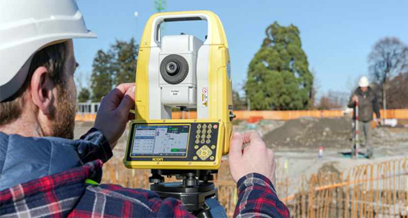 Construction workers work on outdoor building construction site with a Leica iCON iCB50 manual total station and a construction mini prism pole.